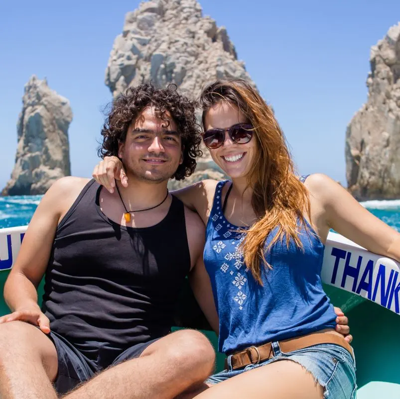 a happy couple posing on a boat in from of the arch at los cabos