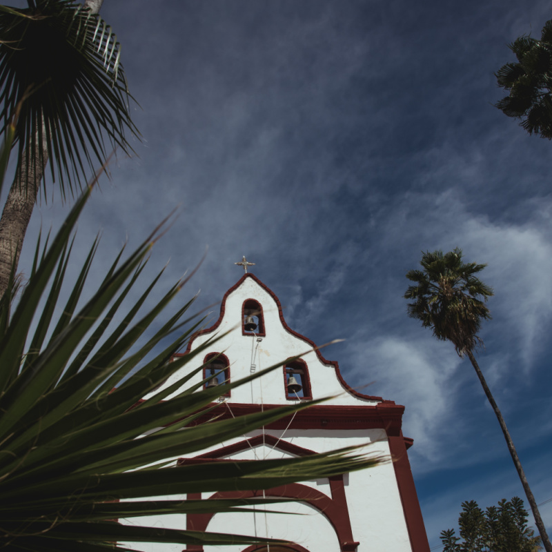 Low-angle-view-of-Miraflores-Church-seen-from-behinh-a-palm-leave.-East-Cape-region-of-Los-Cabos