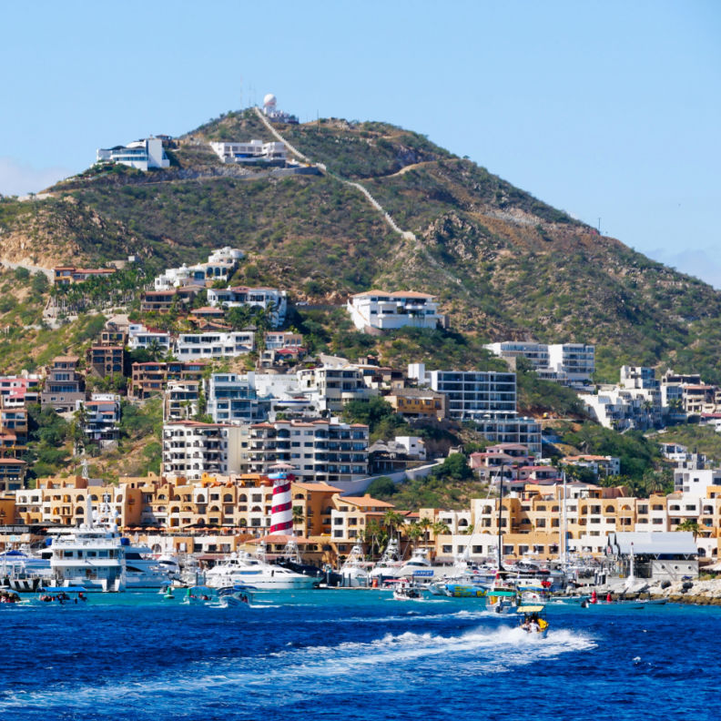 boats in the bay of Cabo San Lucas on a sunny day with accommodations in the distance seen from the sea
