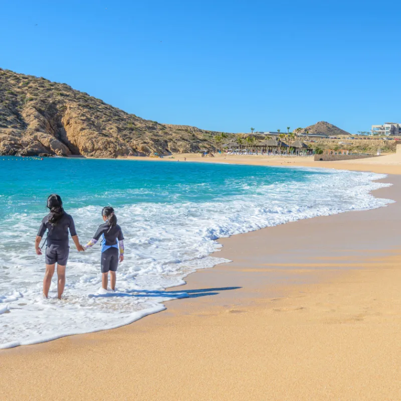 2 young people standing at the waters edge on a los cabos beach