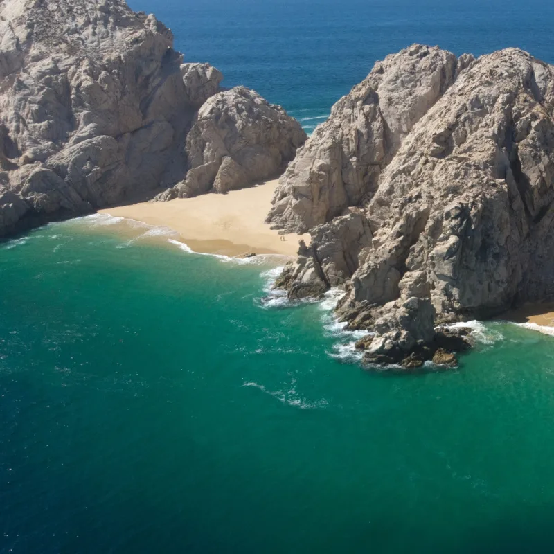 Aerial Image of breathtaking Lovers Beach Playa de los Almantes in Cabo San Lucas, Baja California, Mexico. Impressive rocky cliffs and crystal clear turquoise green water with white sand and waves.