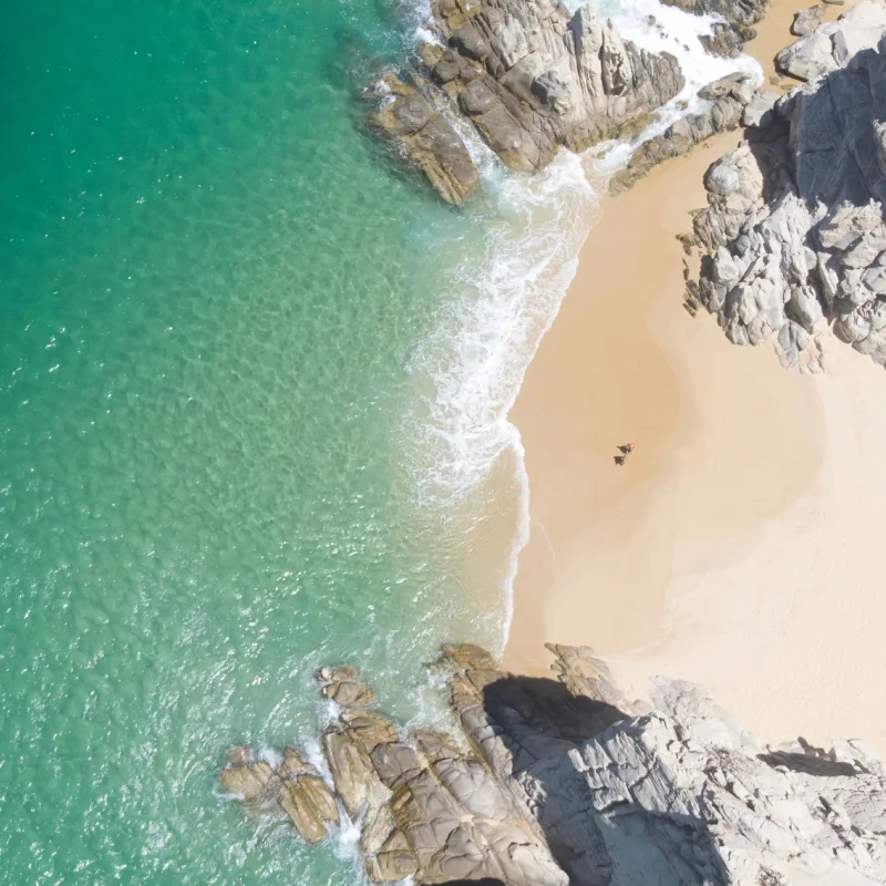 Aerial Image of couple standing on Playa de los Almantes in Cabo San Lucas, Baja California, Mexico. Impressive rocky cliffs and crystal clear turquoise green water with white sand and waves