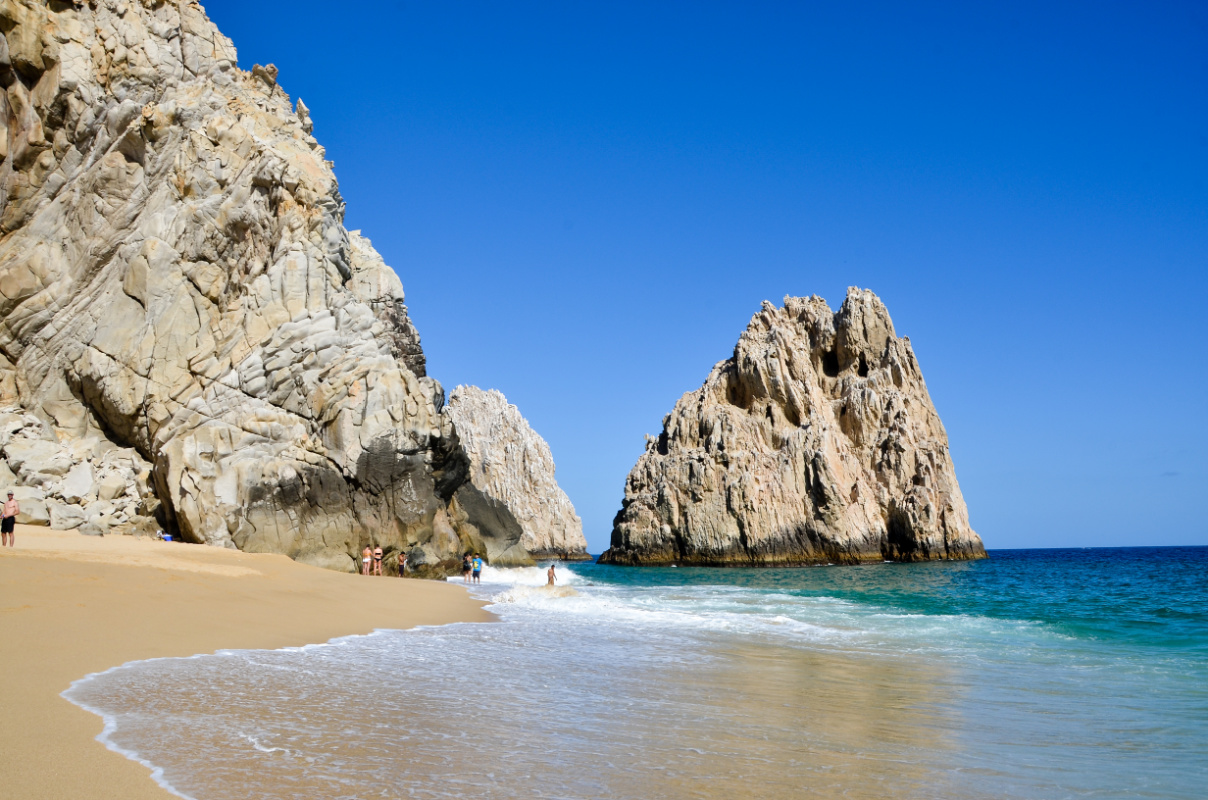 View of beautiful beach in Los Cabos with limestone rock formation and tourists