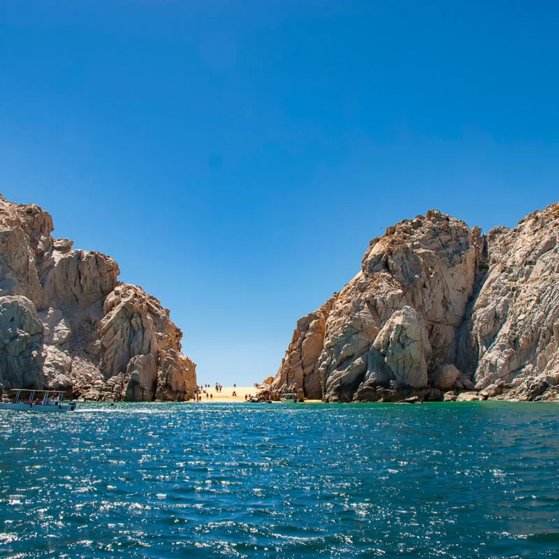 Lover Beach in Los Cabos on a sunny day with tourists enjoying the beach and cliffs on both sides