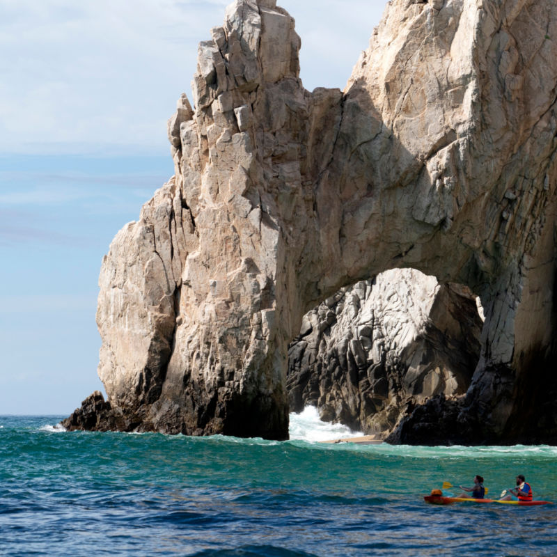 Two people on a canoe approaching the famous El Arco on a sunny day in Los Cabos
