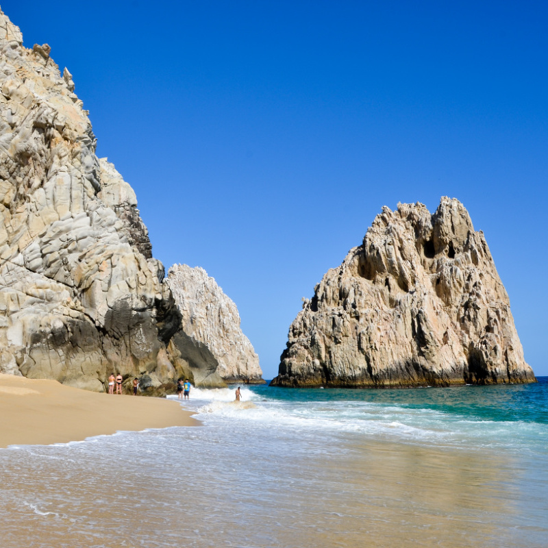 View of beautiful beach in Los Cabos with limestone rock formation and tourists