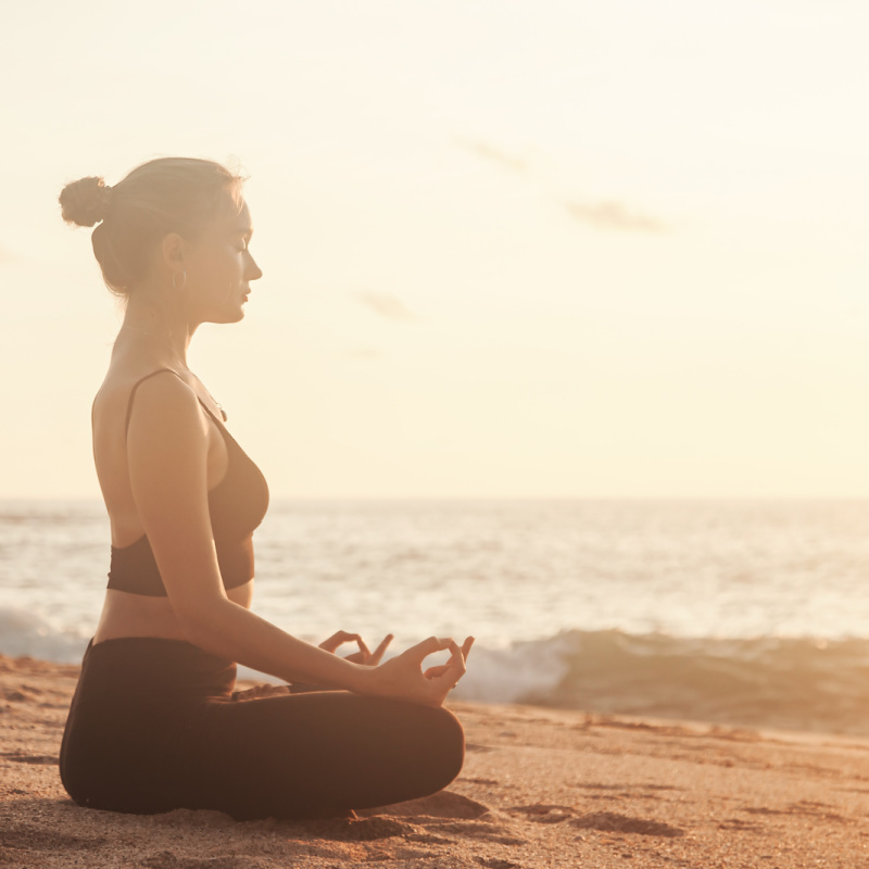 A woman in a yoga pose on a beach at sundown