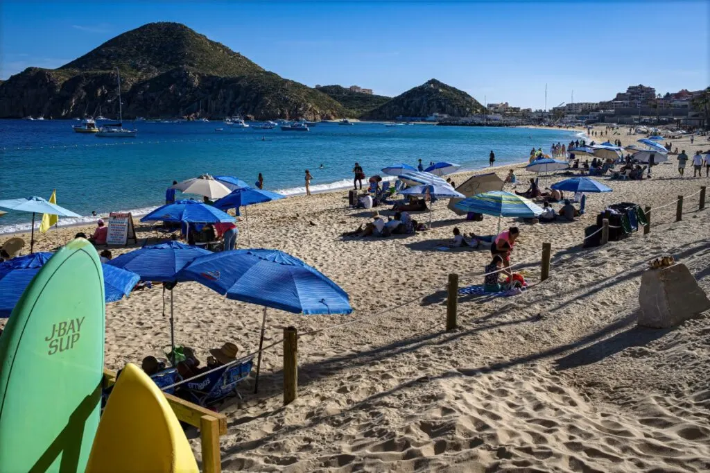 View of popular Medano Beach with beach umbrellas and surfboards, in the heart of downtown Cabo San Lucas.