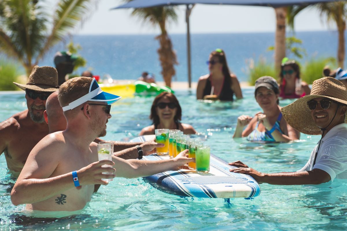 Travelers lifting cocktails from a surfboard in a resort pool