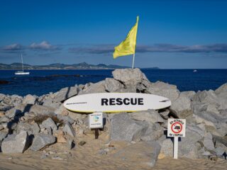 Photo of lifeguard rescue surfboard with yellow warning flag and no camping sign at Palmilla Beach