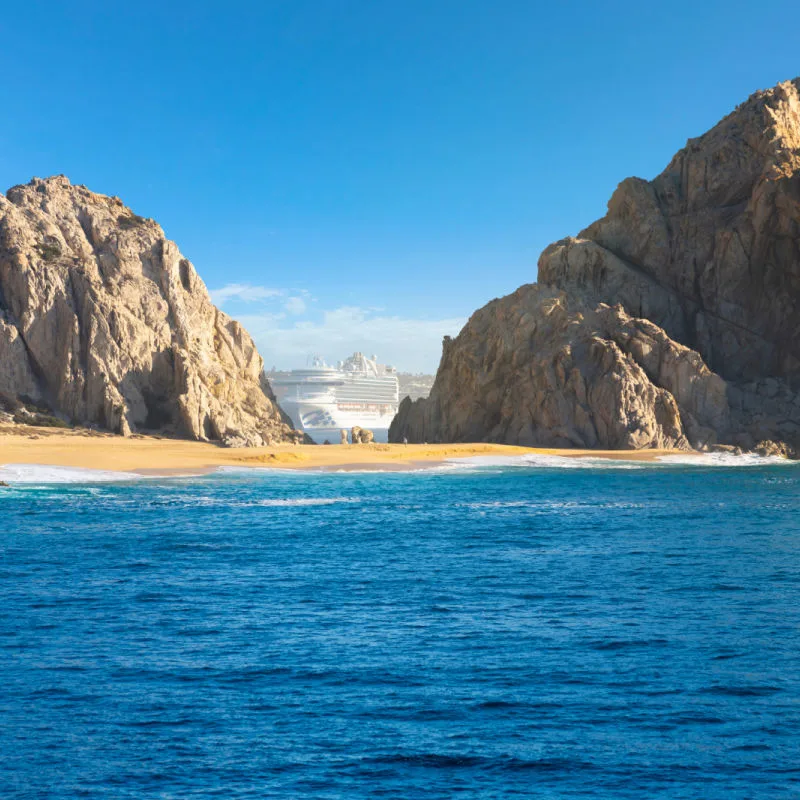 A popular beach in Los Cabos with rock formation and a cruise in the background
