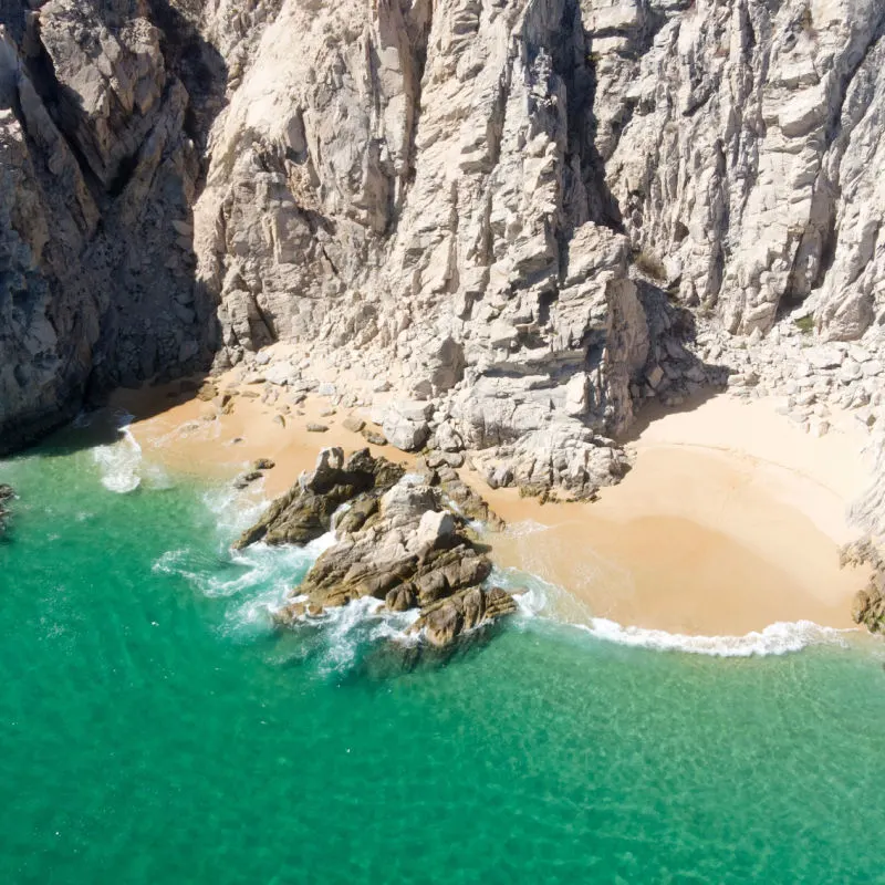Aerial Image of breathtaking Playa de los Almantes in Cabo San Lucas, Baja California, Mexico. Impressive rocky cliffs and crystal clear turquoise green water with white sand and waves. Secret bay
