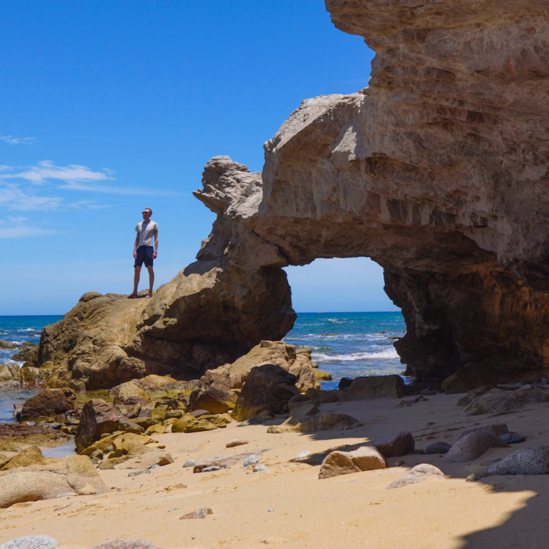 Man standing on rock arch in Los Cabos