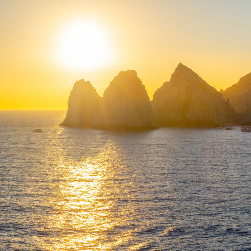 The late afternoon sun starts to set over the El Arco coastal rocks as boats float nearby at the Mexican port city of Cabo San Lucas, Mexico.