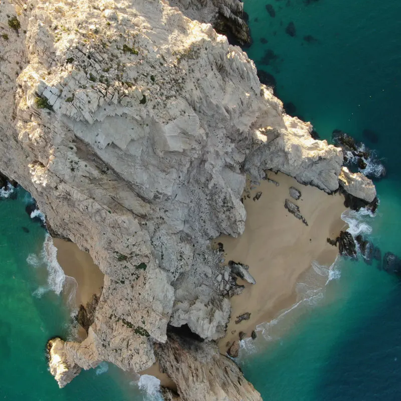 Top down aerial of stone arch and rocky cliffs in Cabo San Lucas, Mexico at sunset with blue waters