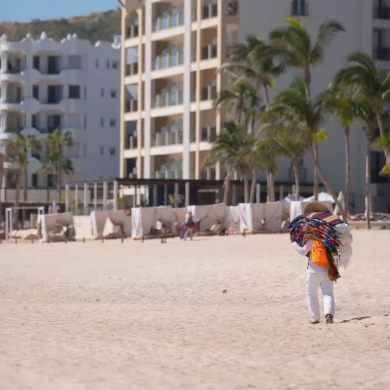 A blanket vendor carries his his colorful blankets on his back to sell to tourists on the beach in Los Cabos Mexico.