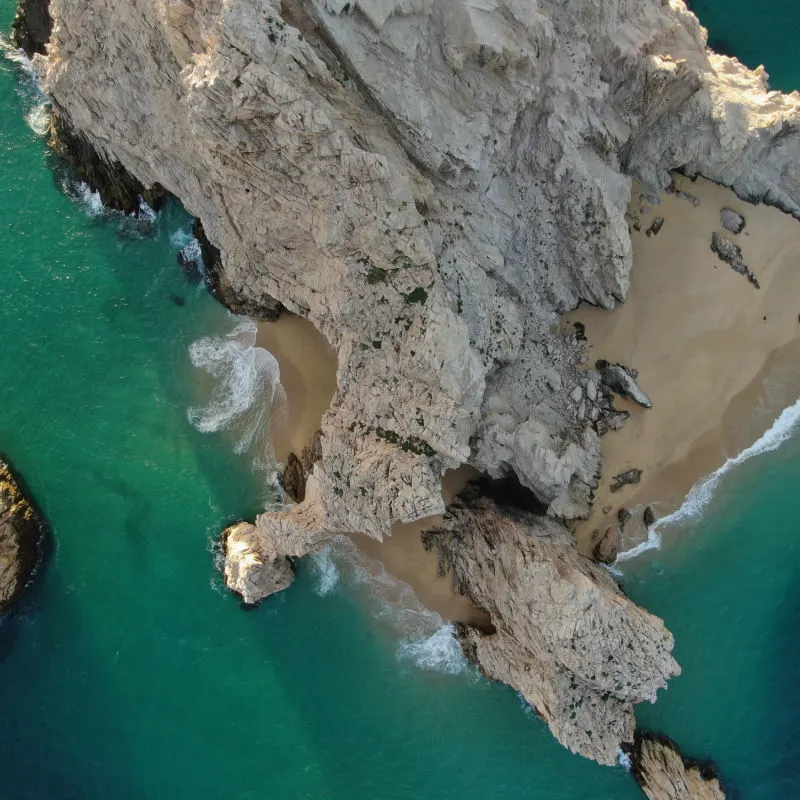Top down aerial of stone arch and rocky cliffs in Cabo San Lucas, Mexico at sunset