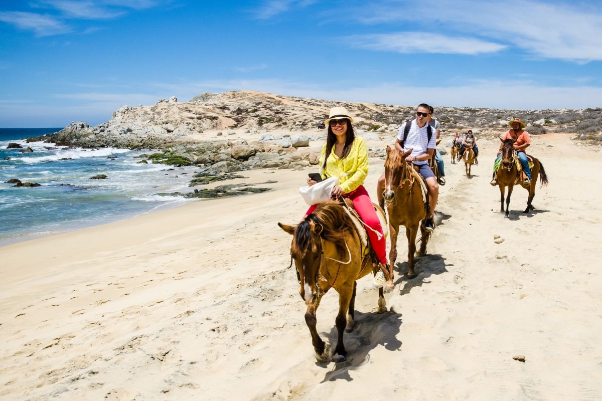 Tourists horseback riding on the beach in Cabo San Lucas, Baja California.
