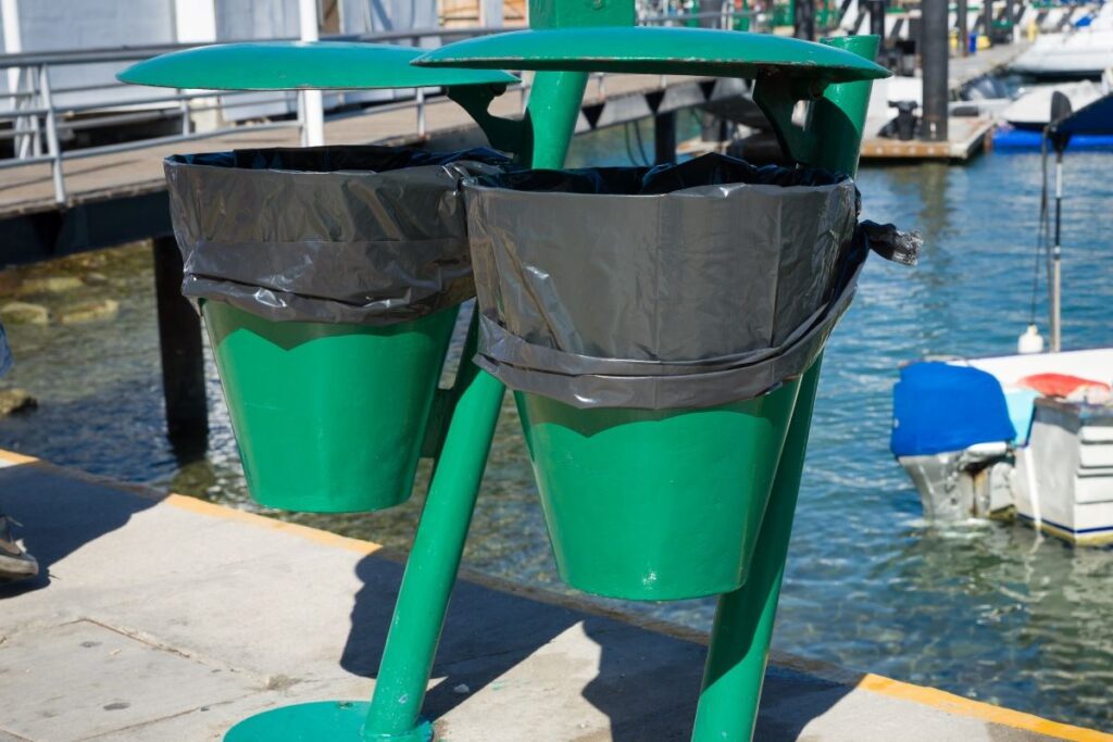 Two green trash cans lined with trash bags mounted on a pier in Cabo San Lucas, Mexico