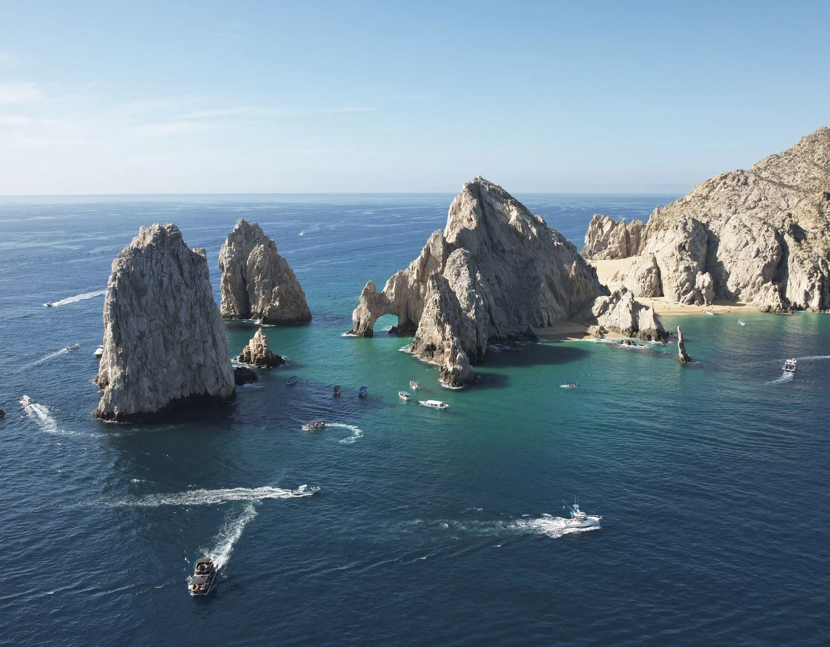 yachts sailing in the sparkling blue waters of the sea against the backdrop of the famous Cabo San Lucas arch in Mexico