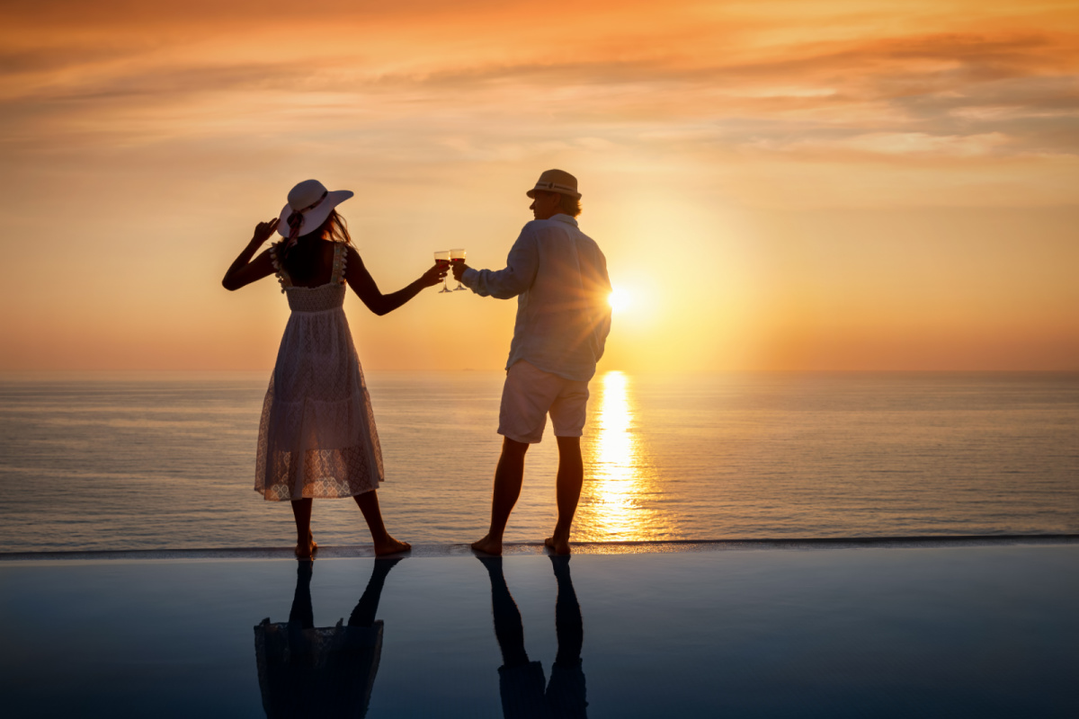 Couple on an infinity pool clinking glasses at sunset