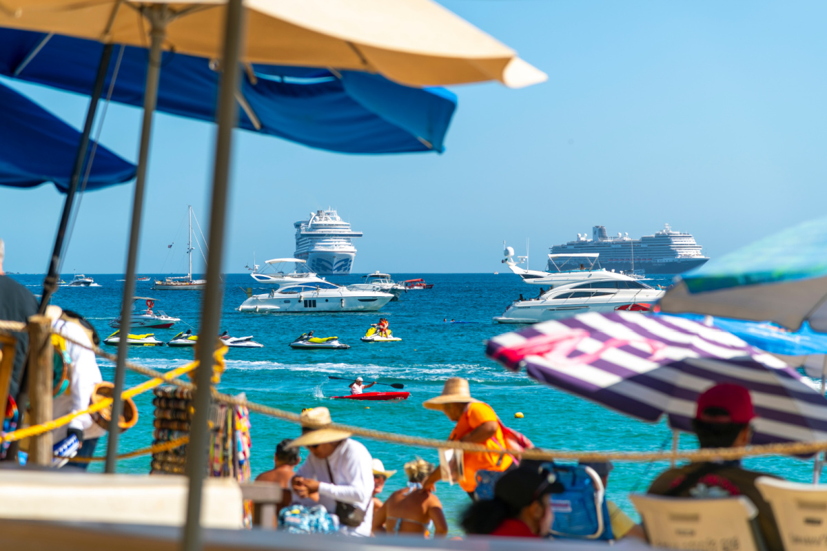 Cabo San Lucas, Mexico: Cruise ships, jet skis, sailboats, yachts and motorboats can be seen at sea through a colorful beachfront scene along the coast of Cabo San Lucas, Mexico.