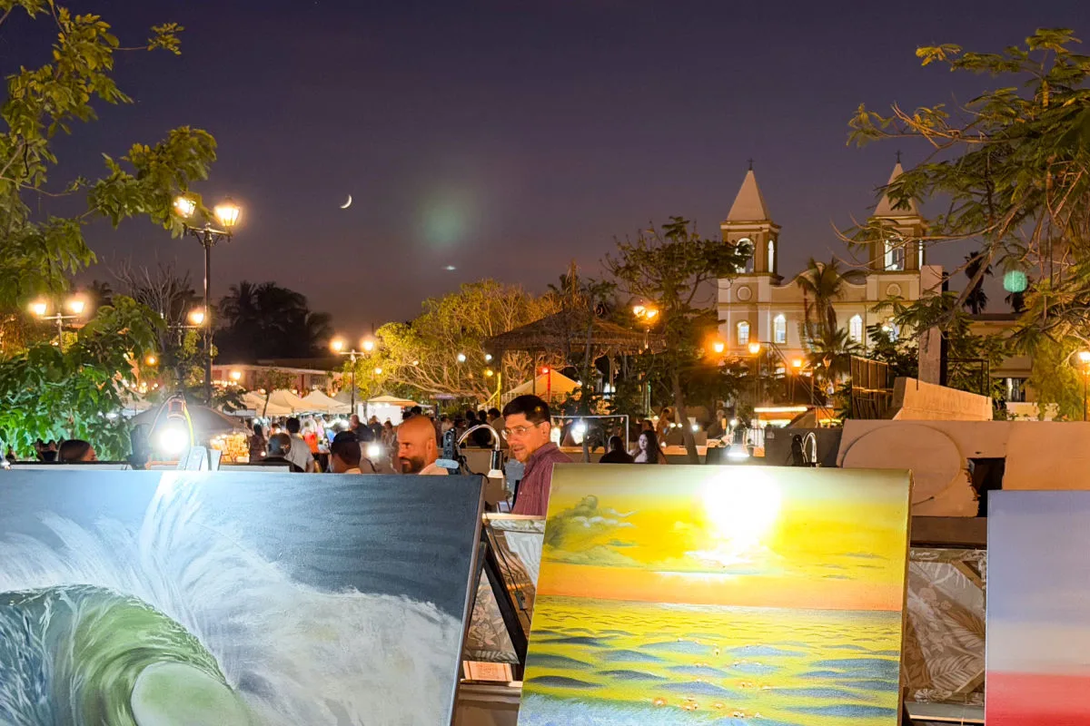 San Jose Del Cabo Art Walk at night with paintings in the foreground and church and moon in the background