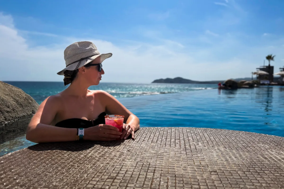 American Woman in infinity pool in Los Cabos overlooking beautiful landscape in the background