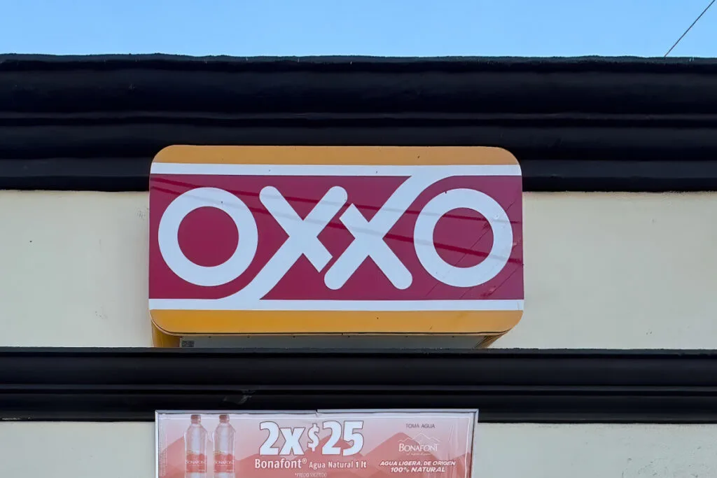 An OXXO convenience store sign with a red and white logo against a yellow background. Below the sign, there's an advertisement for Bonafont