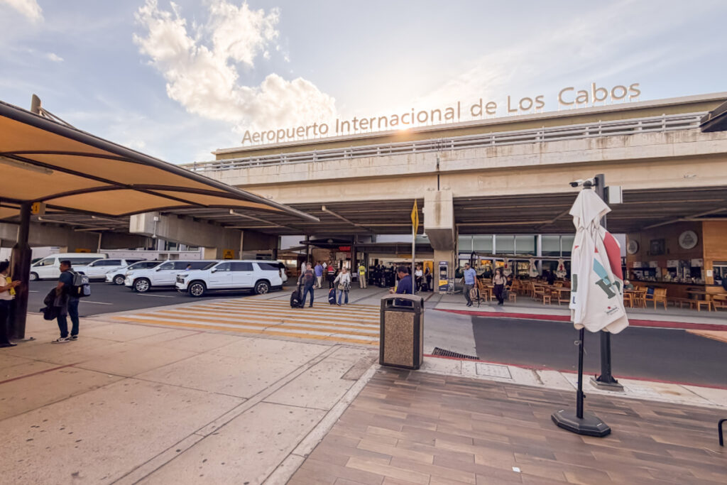 Terminal 2 Arrival Area Los Cabos International Airport with sun peaking out behind the sign and tourists exiting airport