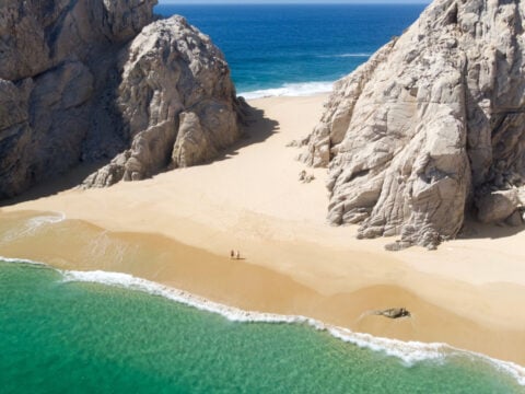 Aerial Image of couple standing on Playa de los Almantes in Cabo San Lucas, Baja California, Mexico. Impressive rocky cliffs and crystal clear turquoise green water with white sand at lover beach.